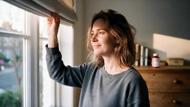 Best morning drink for bloating: a woman opening the blinds in her bedroom at dawn