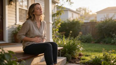 Woman sits outdoors with a hand on her abdomen, illustrating estrogen bloating discomfort across the cycle.